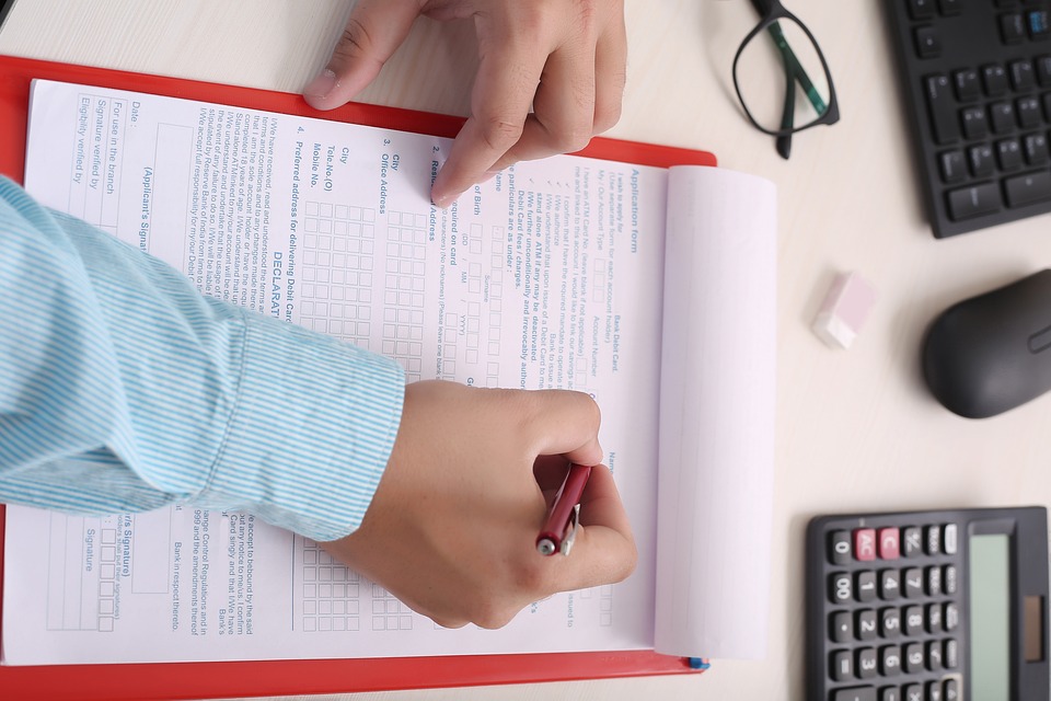 Kuvassa kädet ja oikeassa kädessä kynä jolla täyttää asuntohakemusta.